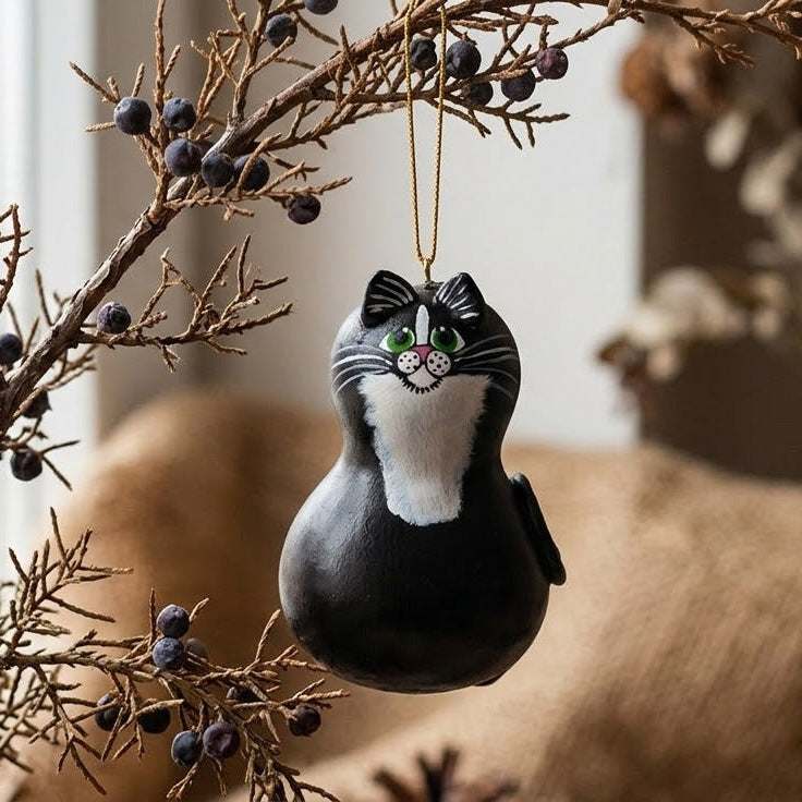 Decorative ornament shaped like a cat hanging on a branch with berries.