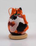 Calico cat gourd art ornament with orange, black, and white colors and green eyes hanging with a hemp cord on a wooden base