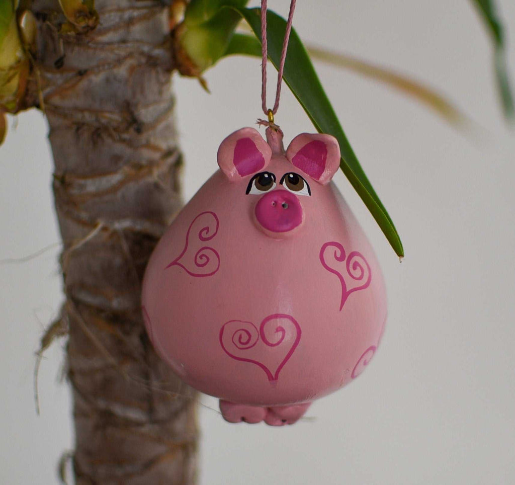 Pink pig ornament with heart designs hanging on a houseplant branch