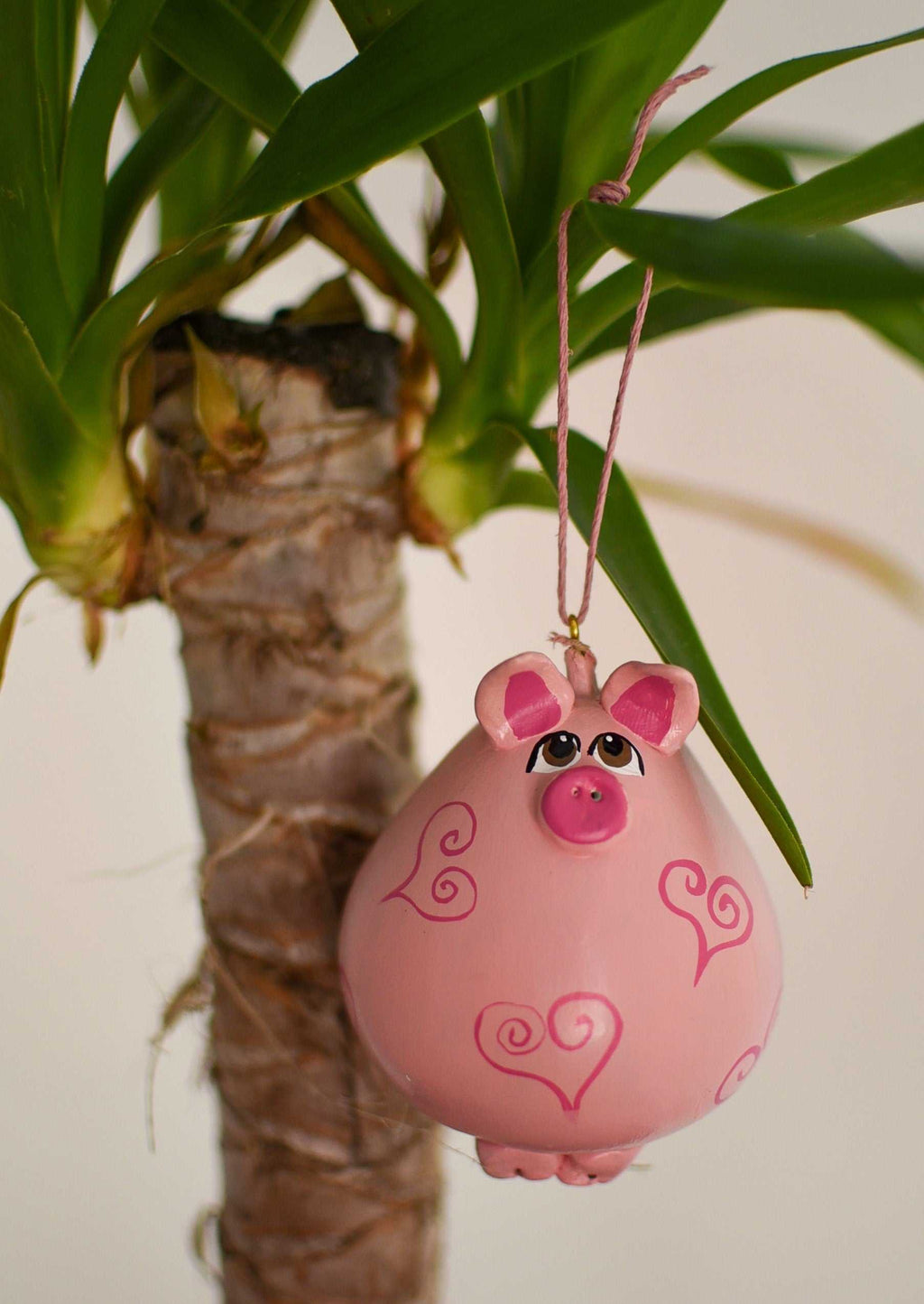 Pink pig ornament with heart designs hanging on houseplant branch