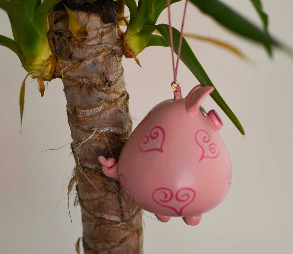 Pink pig ornament with heart designs hanging on a houseplant branch