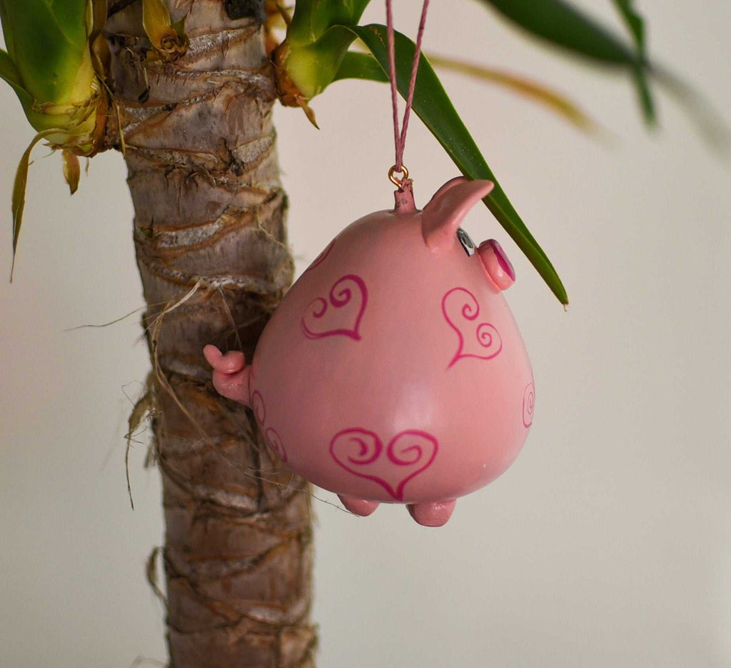 Pink pig ornament with heart designs hanging from a houseplant branch