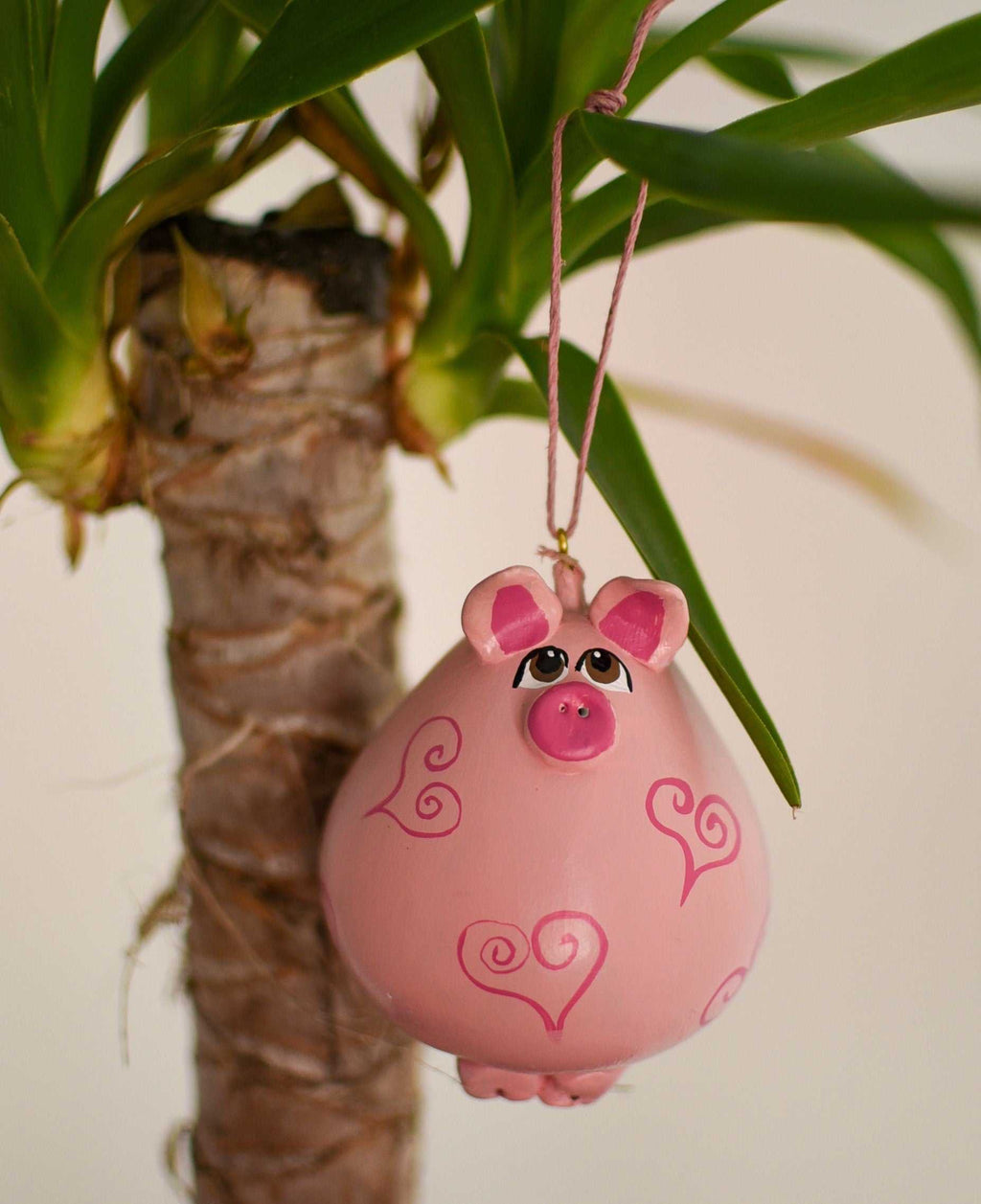 Pink pig ornament hanging from houseplant with heart designs, handcrafted from dried gourd