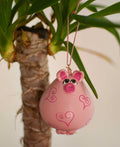 Pink pig ornament hanging from houseplant with heart designs, handcrafted from dried gourd